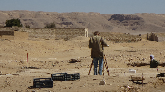 Man standing behind a tripod looking over the archaeological site in Egypt.