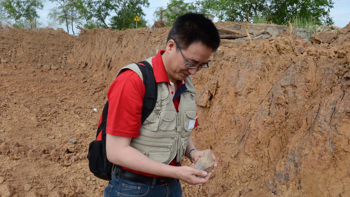 Dr. Chen Shen picking up the hand axe from a site that runs through the newly built highway