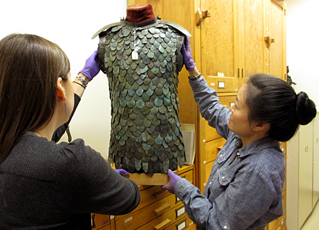 Two women carefully adjust an armour vest on a stand.