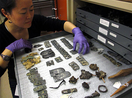 A woman arranges objects inside a metal drawer in the ROM's storage room.