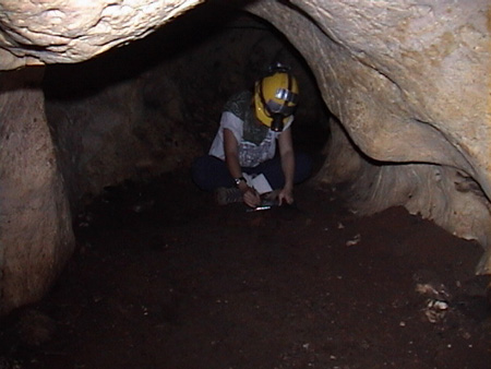 Inside a dark cave, Kay works under the light of her headlamp.