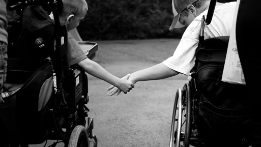 Two kids in wheelchairs holding hands