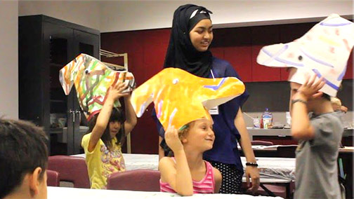 Volunteer supervising children wearing a dinosaur headdresses.