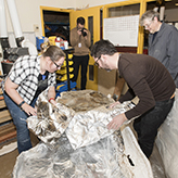 Photo of three people removing foil from a fossil specimen