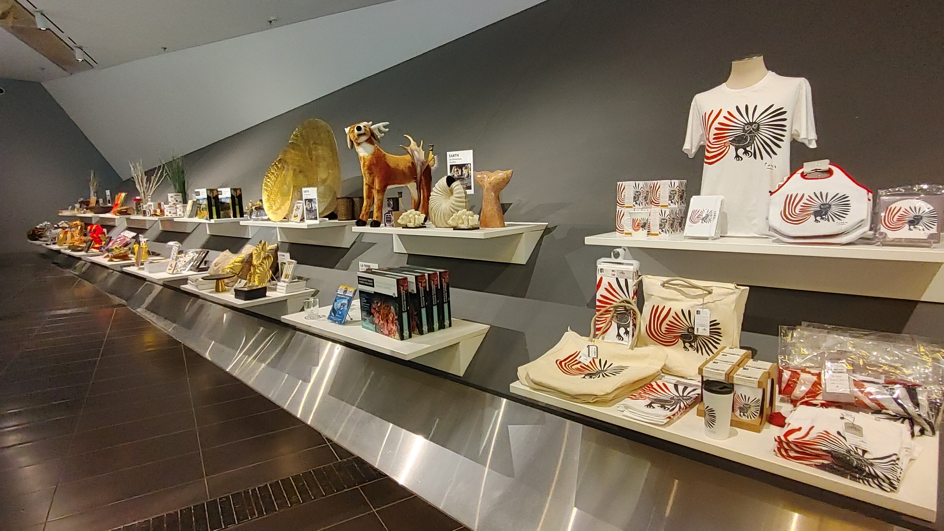 A store display wall showing assorted items including t-shirts, stuffies, homewares, and sculptures. 