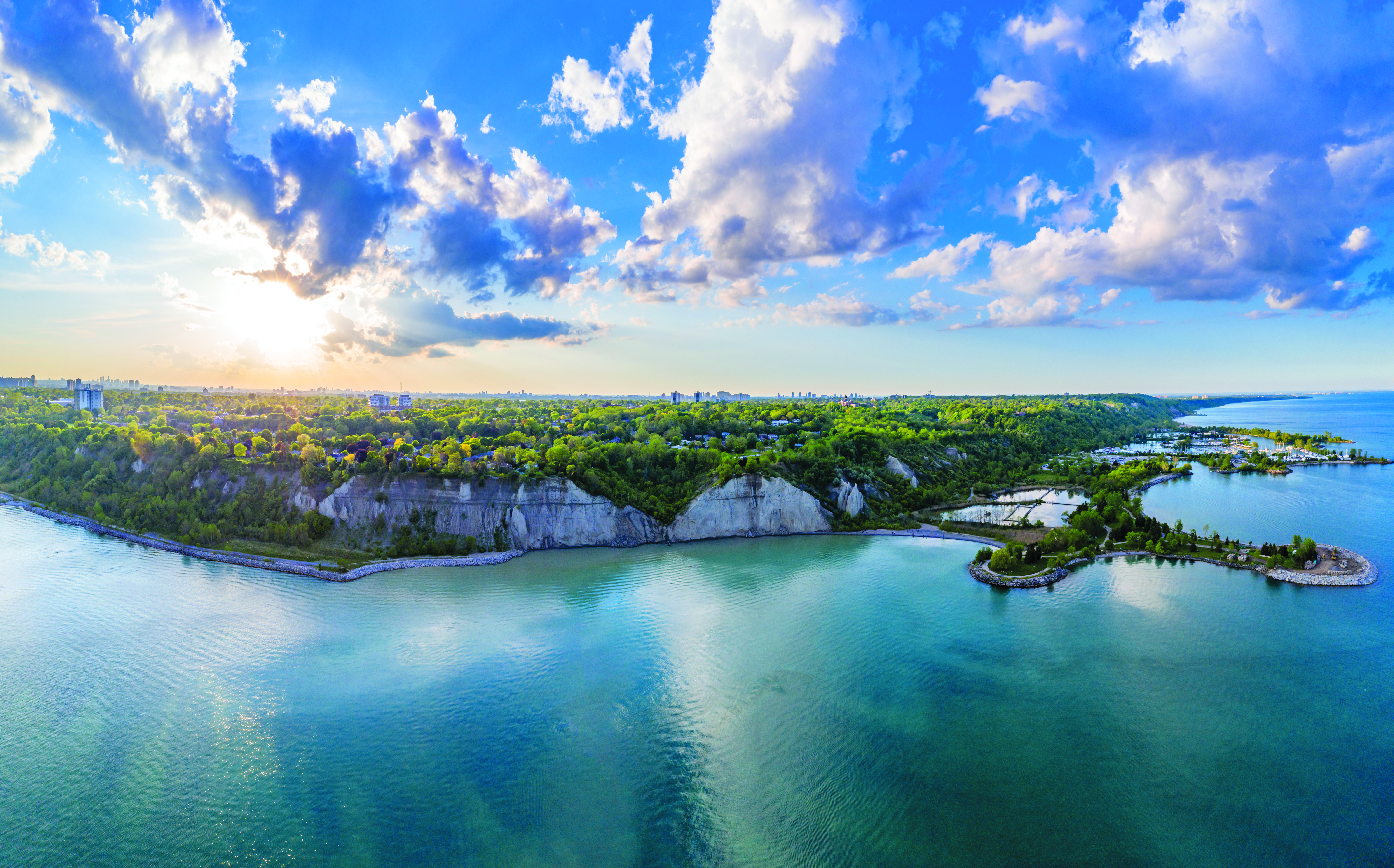 Vue aérienne de l'eau et des collines verdoyantes avec le soleil qui brille derrière les nuages.