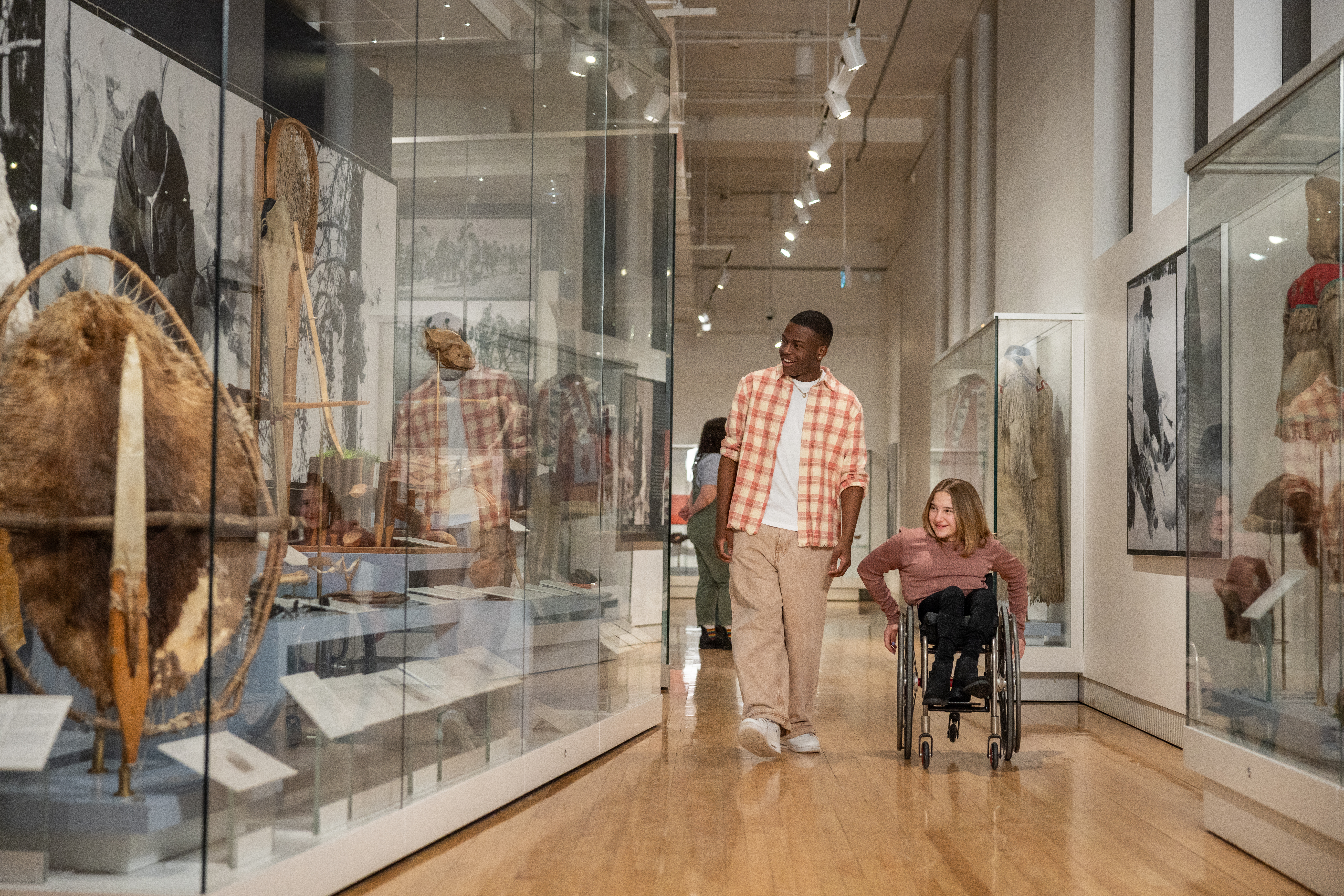 A guy in a plaid shirt walking with a girl in a wheelchair looking at museum collections at ROM