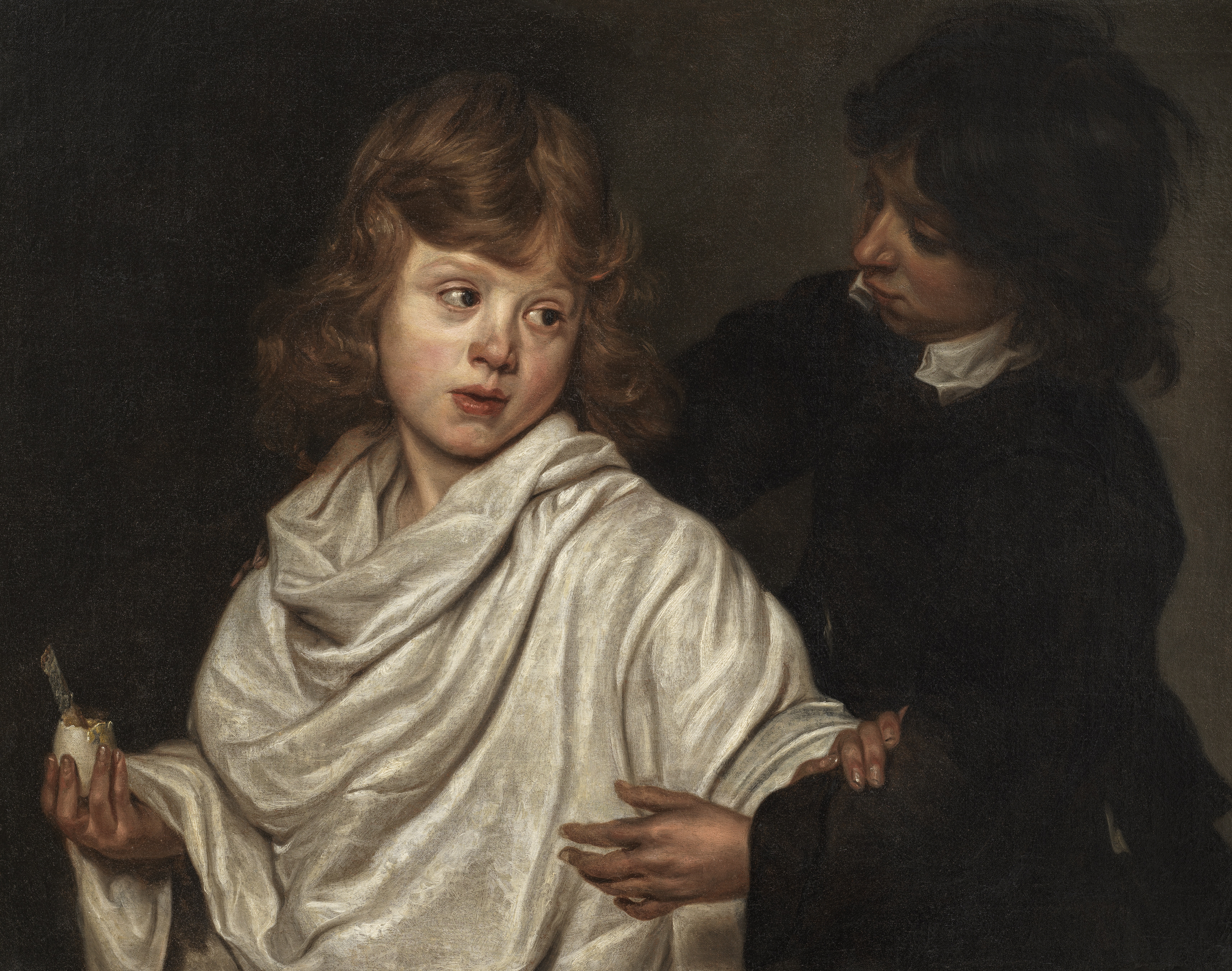 A young boy in a white shirt, holding a boiled egg, pushes another boy, in a black tunic, away from the egg.