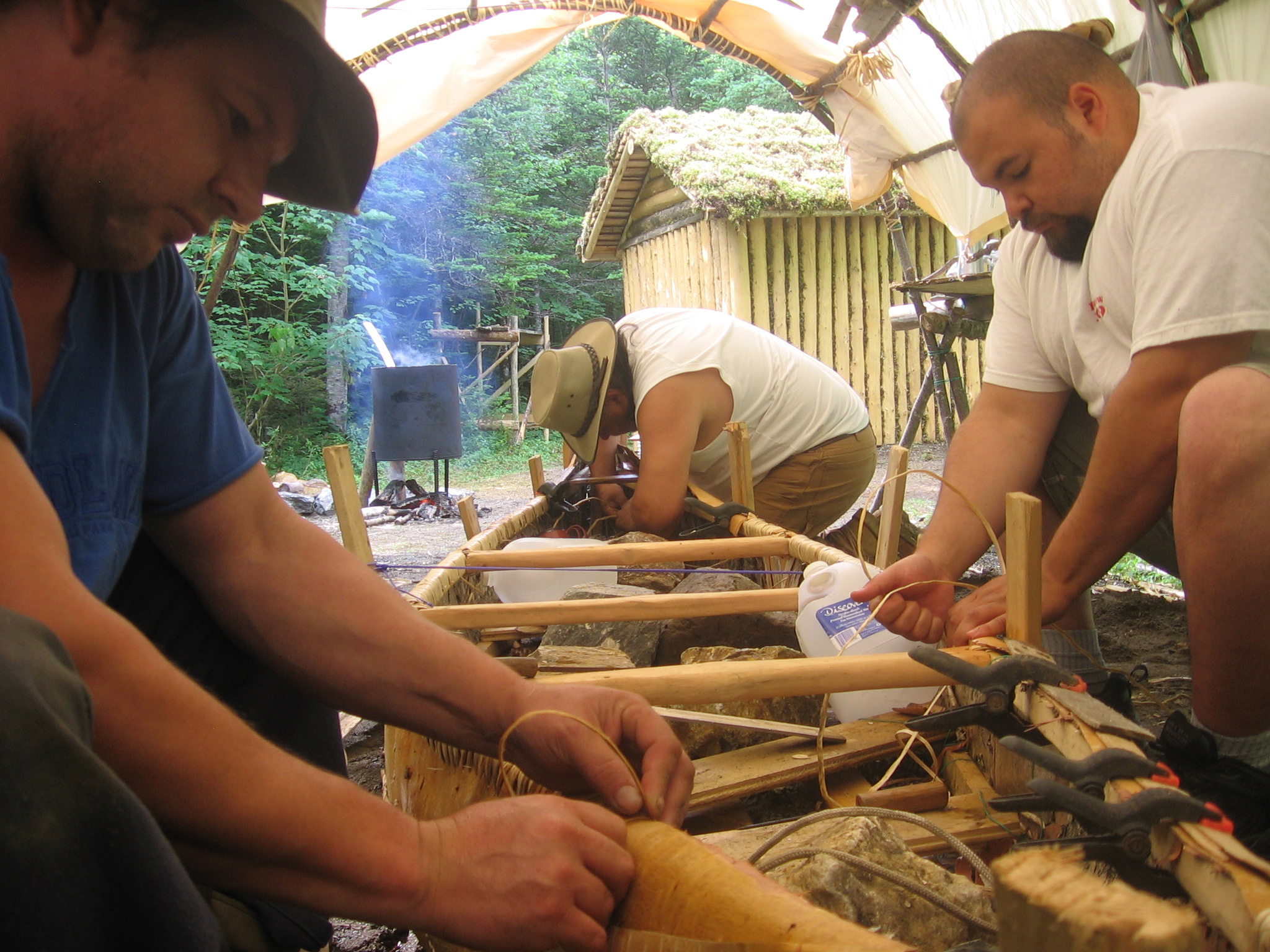 Three men making a birch bark canoe.