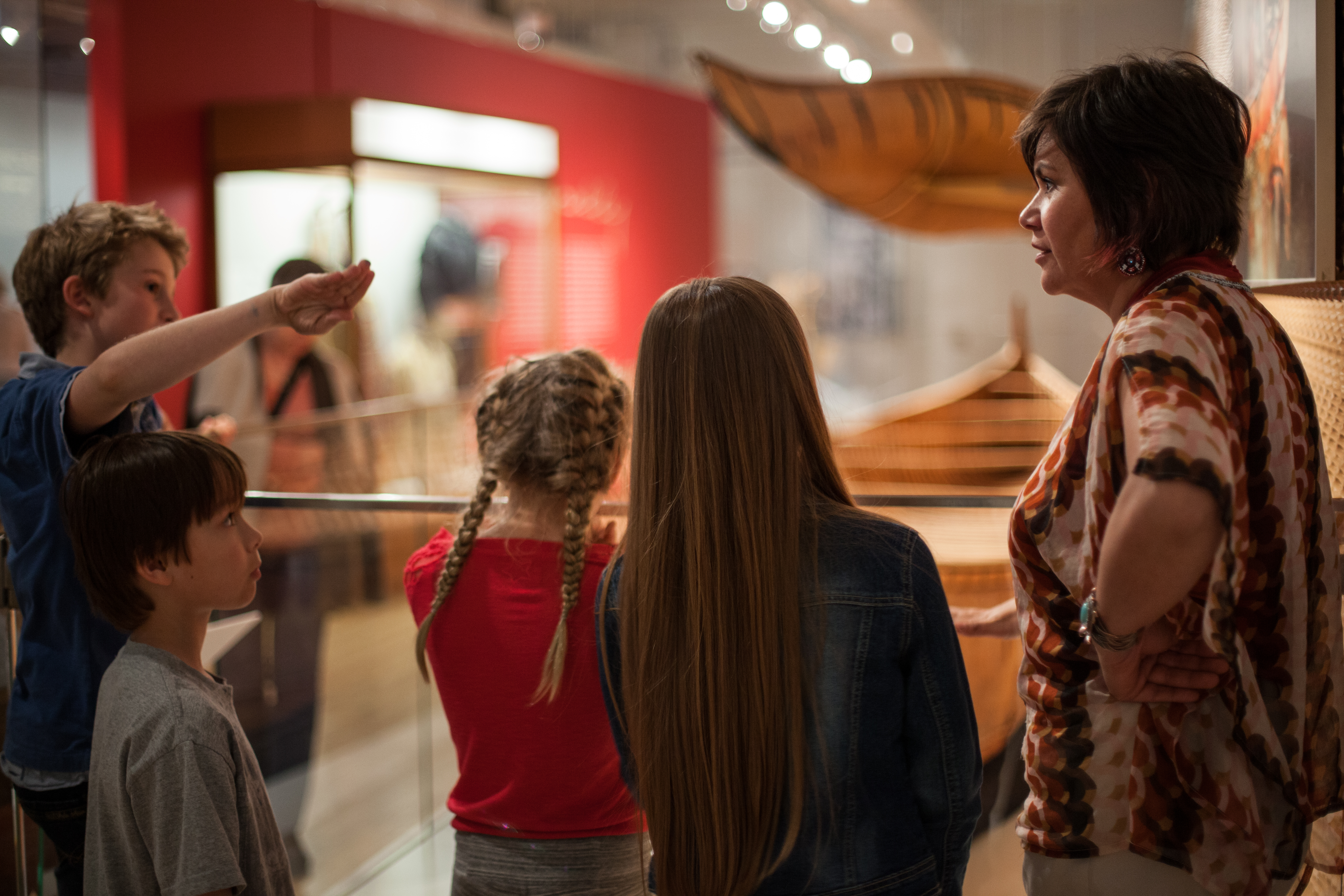 several students and an Indigenous educator stand near a display of birchbark canoes
