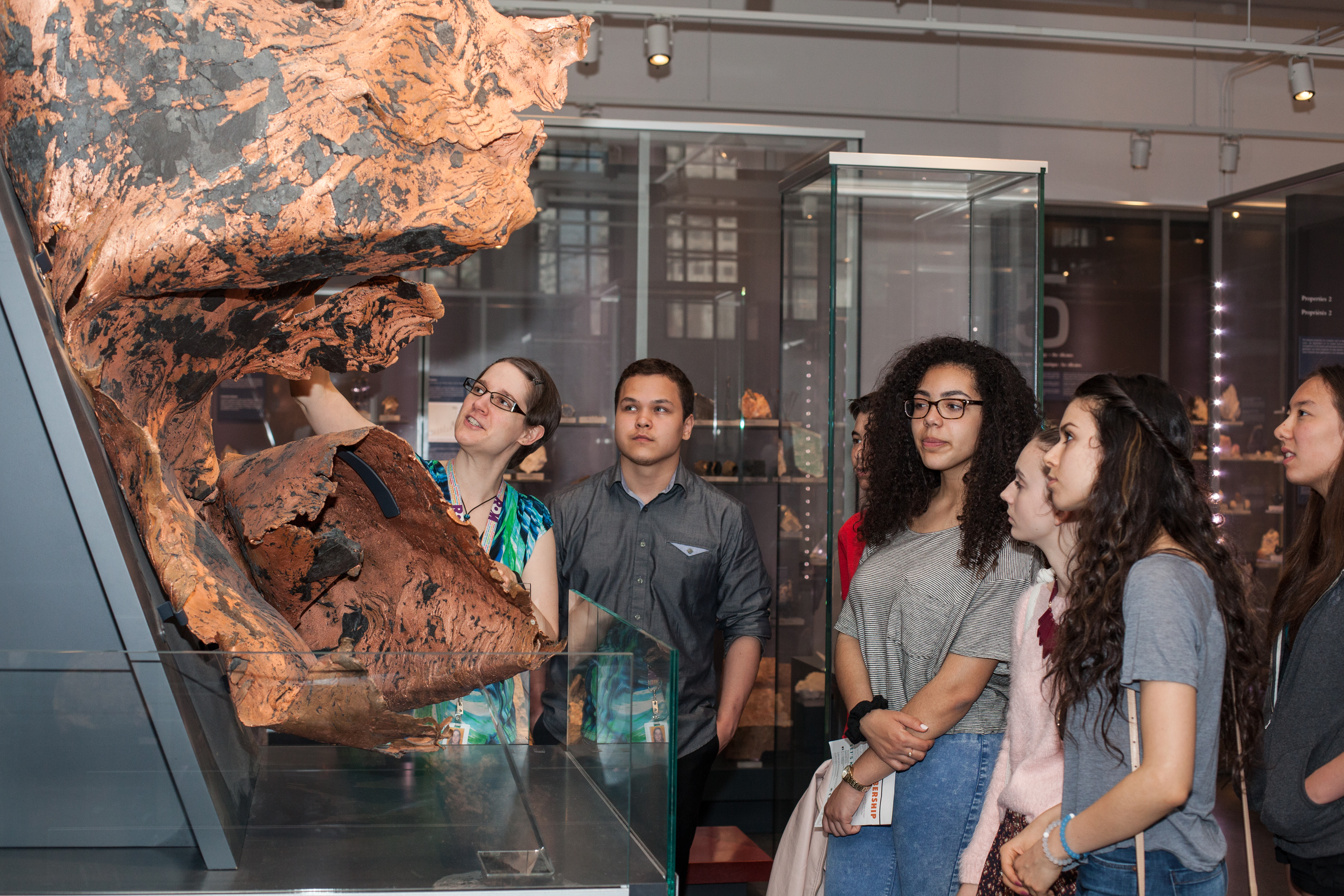 Diverse teenage students examine a twisted sheet of copper with guidance from a teacher