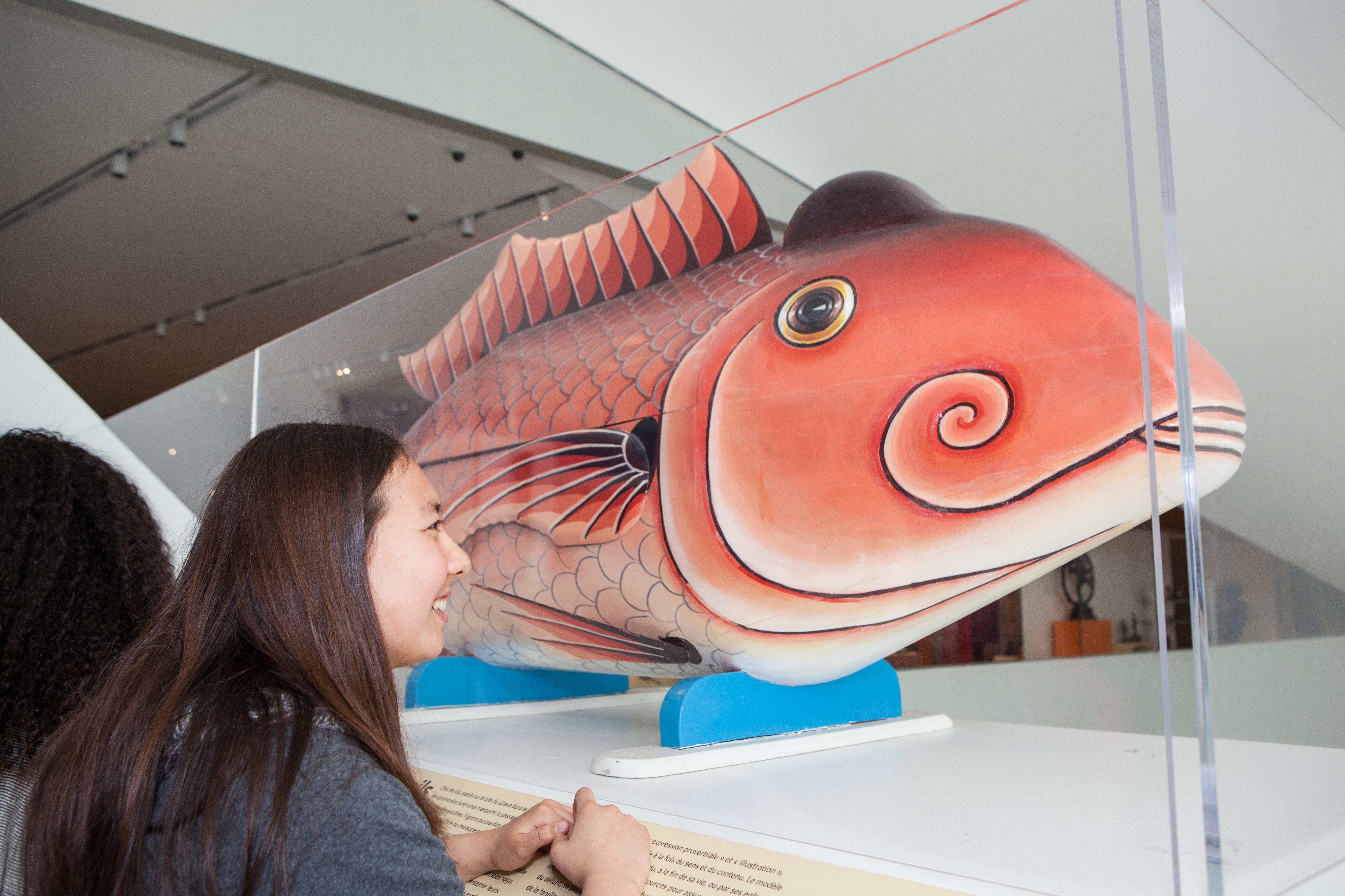 A smiling student looks at a large coffin in the shape of a painted red fish