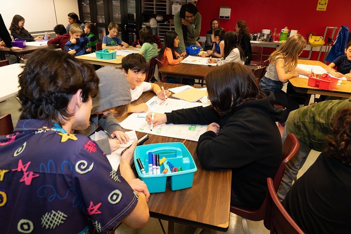 Students sit at tables in the Makerspace using markers to draw paper prototypes of games