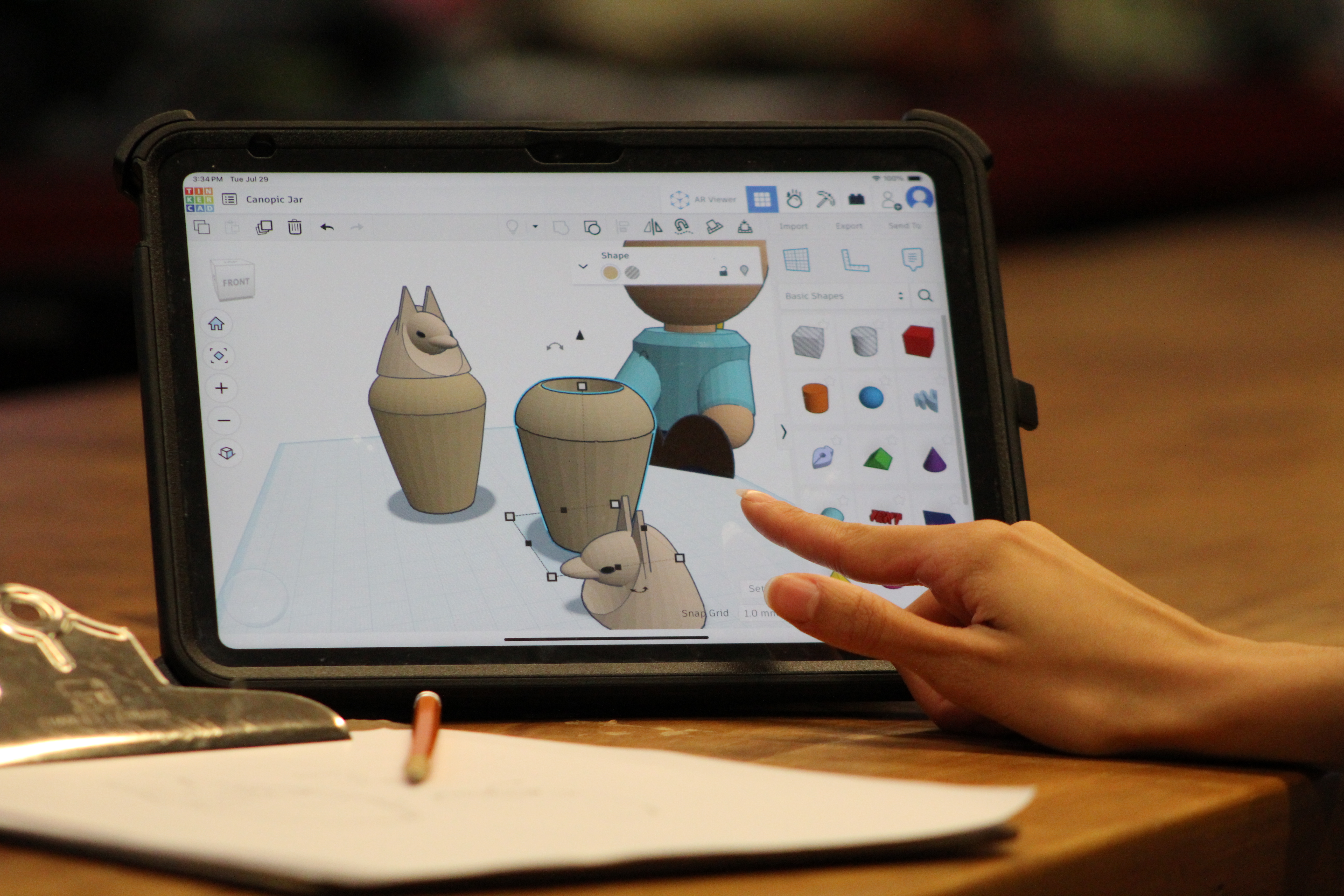 A hand touches an ipad displaying 3D models of Egyptian objects