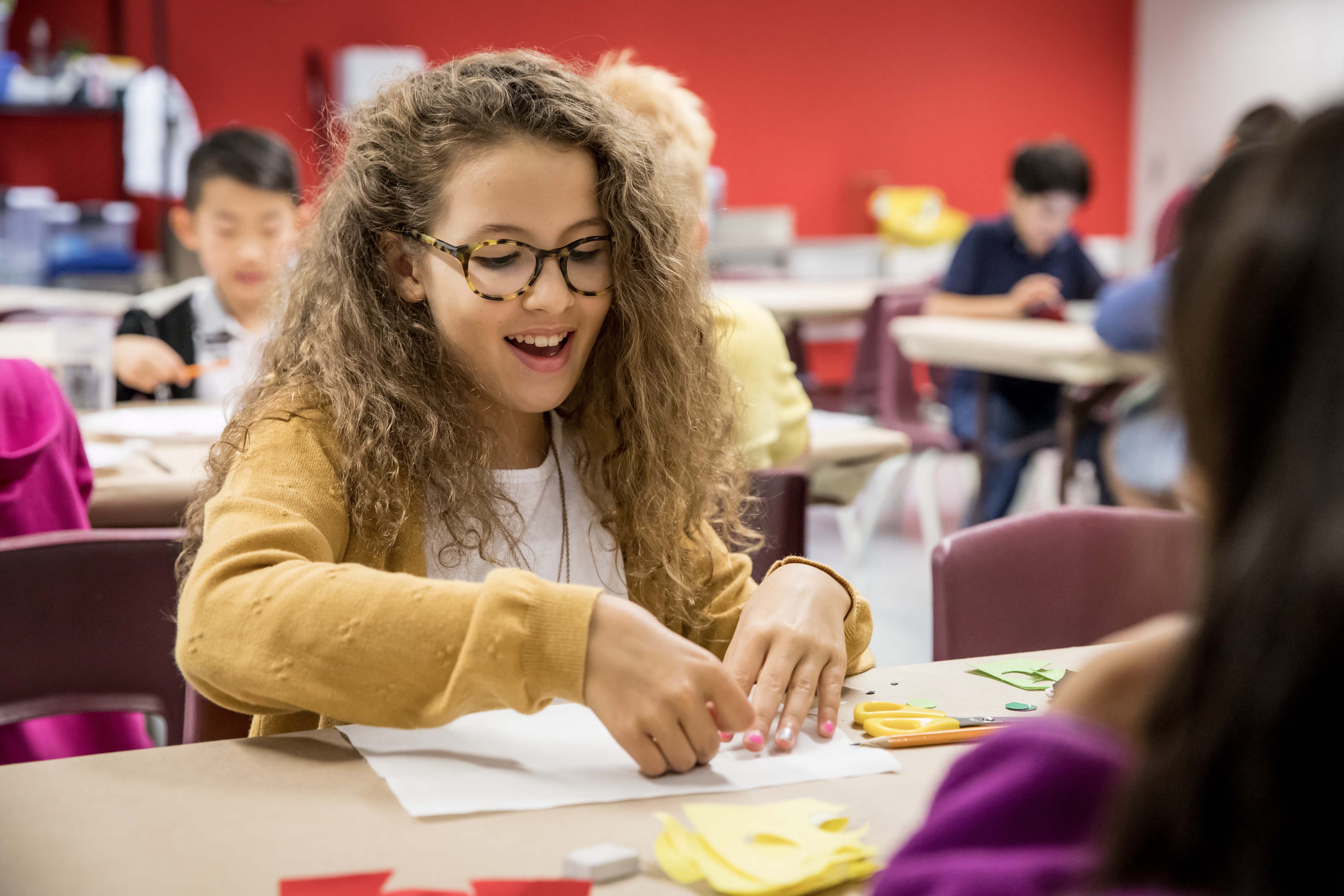 A smiling curly-haired girl holds fabric over a table