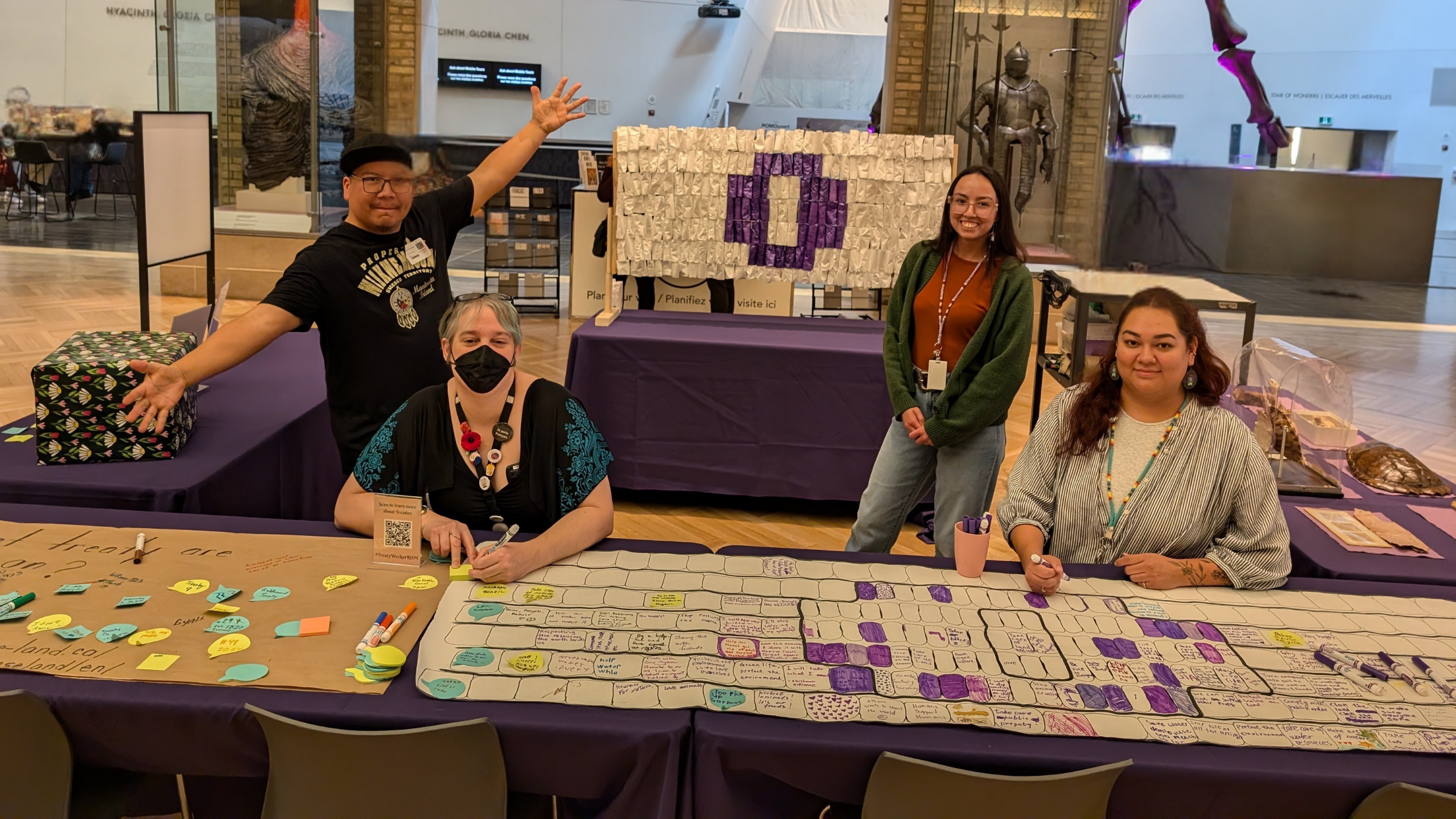 Three indigenous staff members and one white staff member sit at a table full of activities smiling and gesturing around them.
