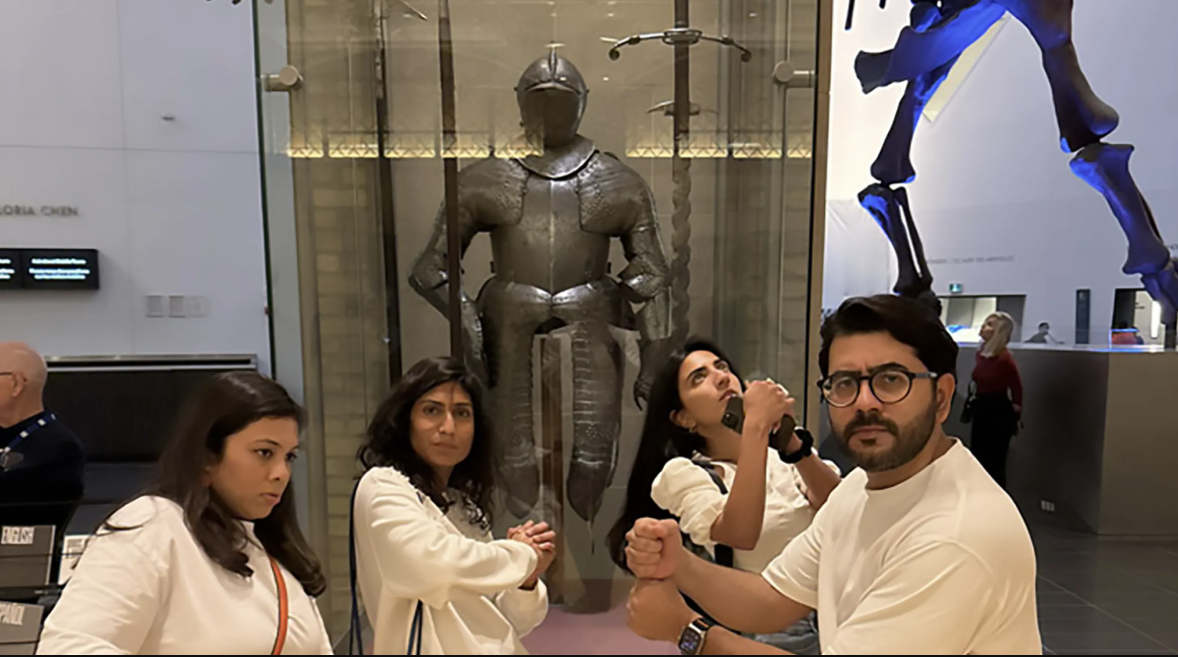 Four people posing in front of a knight's armor.