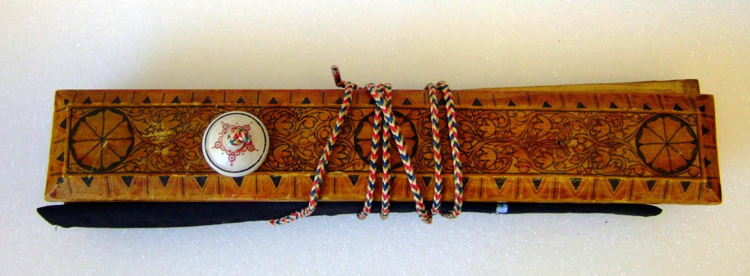 A decorative wooden case featuring circular and botanical designs. A white button on the top of the case secures a red, white ,nad blue cord wrapped around the case.