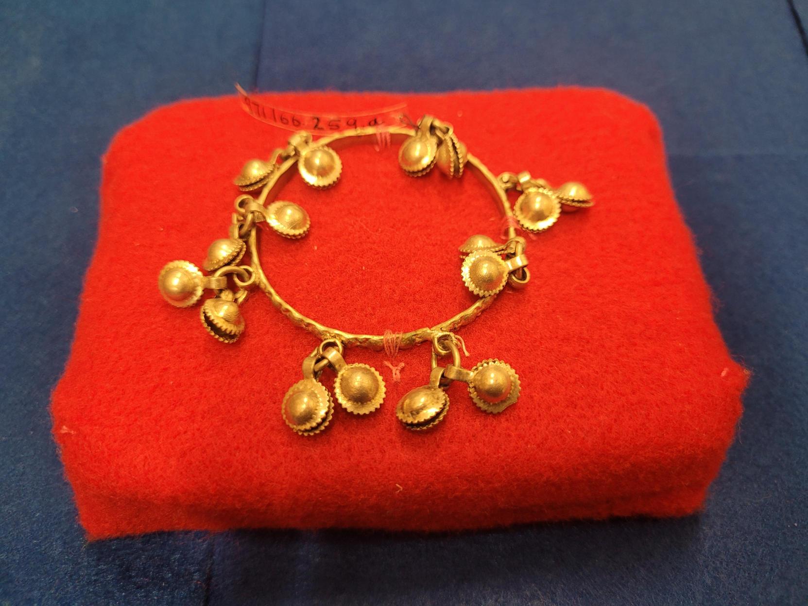 Round silver anklet for children. Thin silver central ring decorated with round silver charms suspended from central ring in eight groups of two. Produces jingling sound when handled or worn.