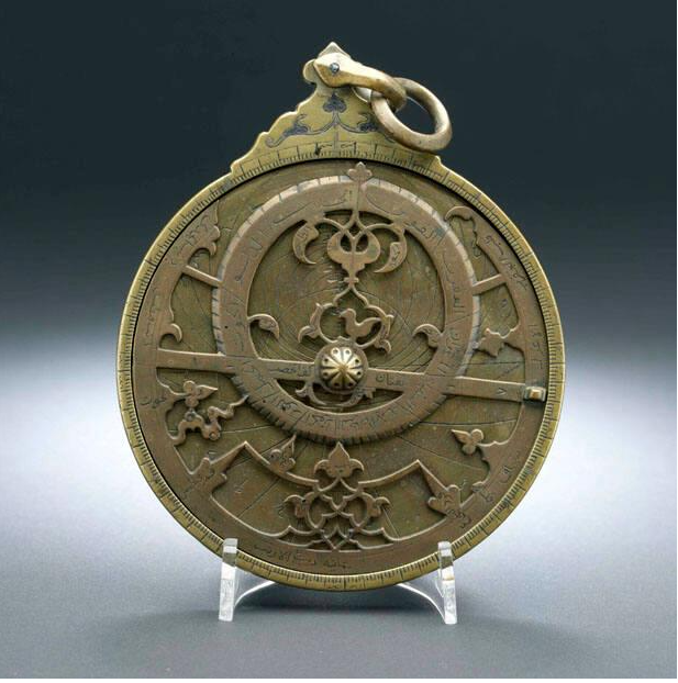 A bronze-coloured disk with carved details including an off-centre ring, leaves, and a small bird. There is a ring at the top similar to a pendant.
