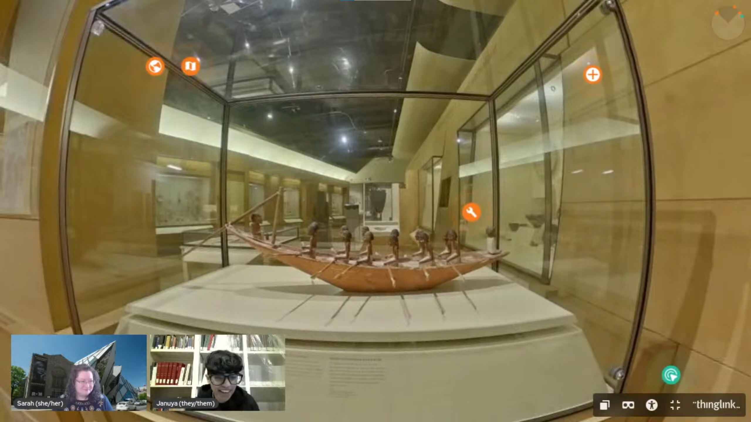 A display showing a wooden model of a boat filled with small humanoid figures with black skin and dark hair. Facecam inserts of two smiling people are at the bottom of the screen.