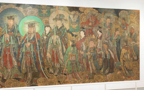 A wide mural painted in bright tones of red, blue, yellow, and turquoise. It shows a procession of deities across a cloudy sky.