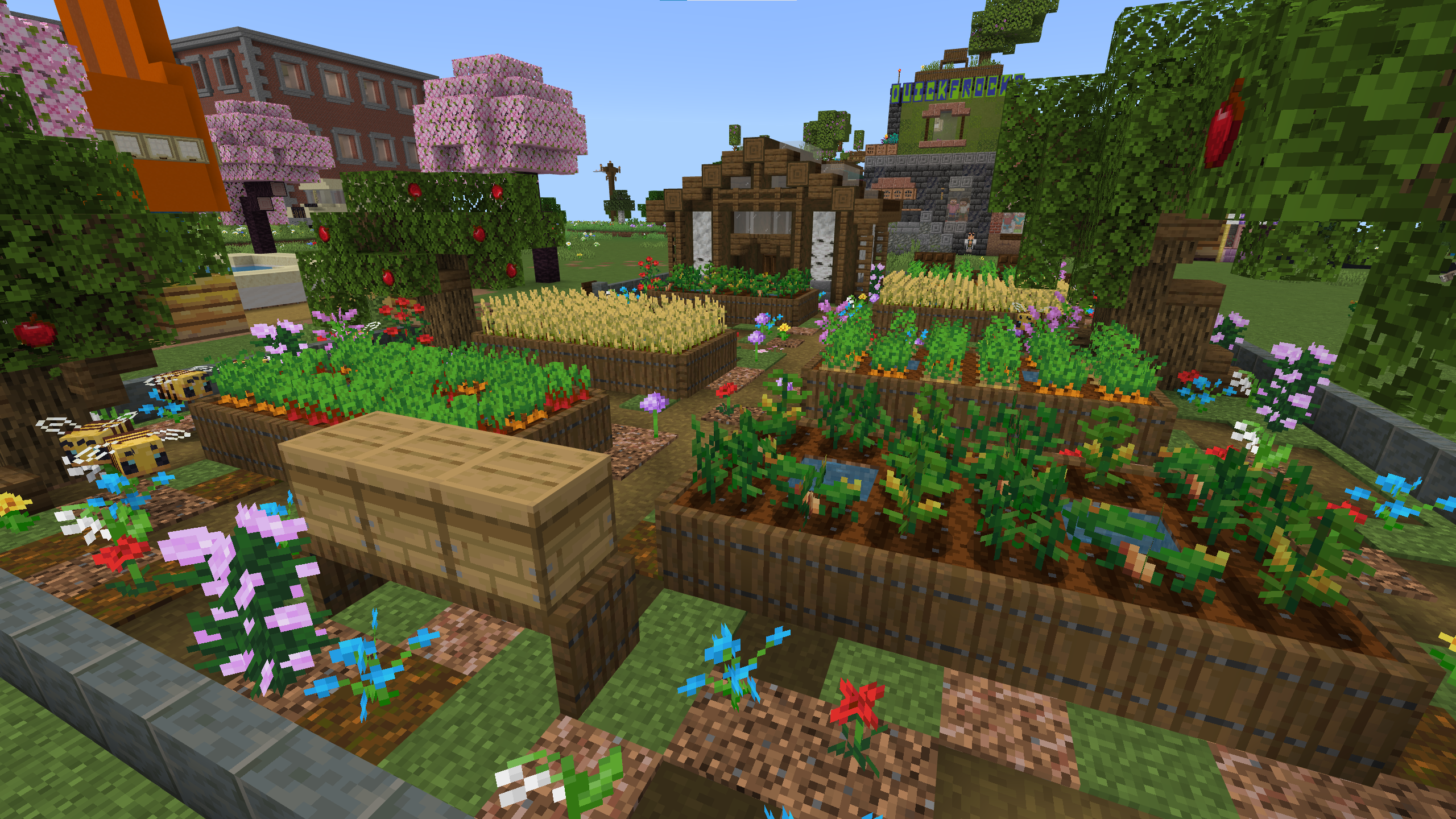A Minecraft screenshot of a garden containing vegetable plots, flowers, beehives, and a greenhouse.