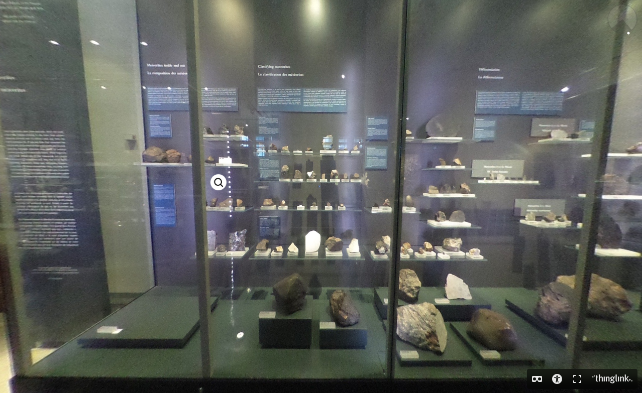 A museum display case containing meteorites of various sizes. Their colour ranges from light gray to black.