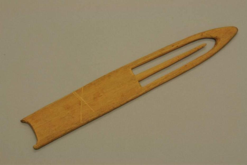 A carved piece of wood with a pointed tip and a pointed needle within a cutout space at the tip.