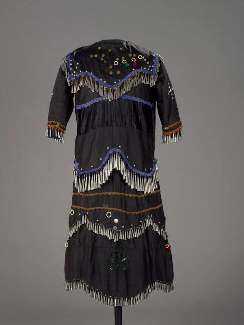 A dress made of dark fabric decorated with many fringes of metal cones.