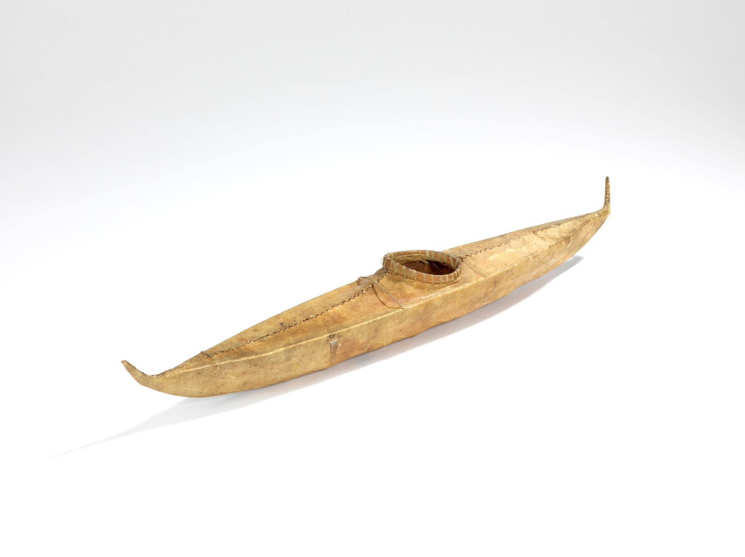 A 43 cm model of a kayak covered in light brown skin sewn together with sinew.