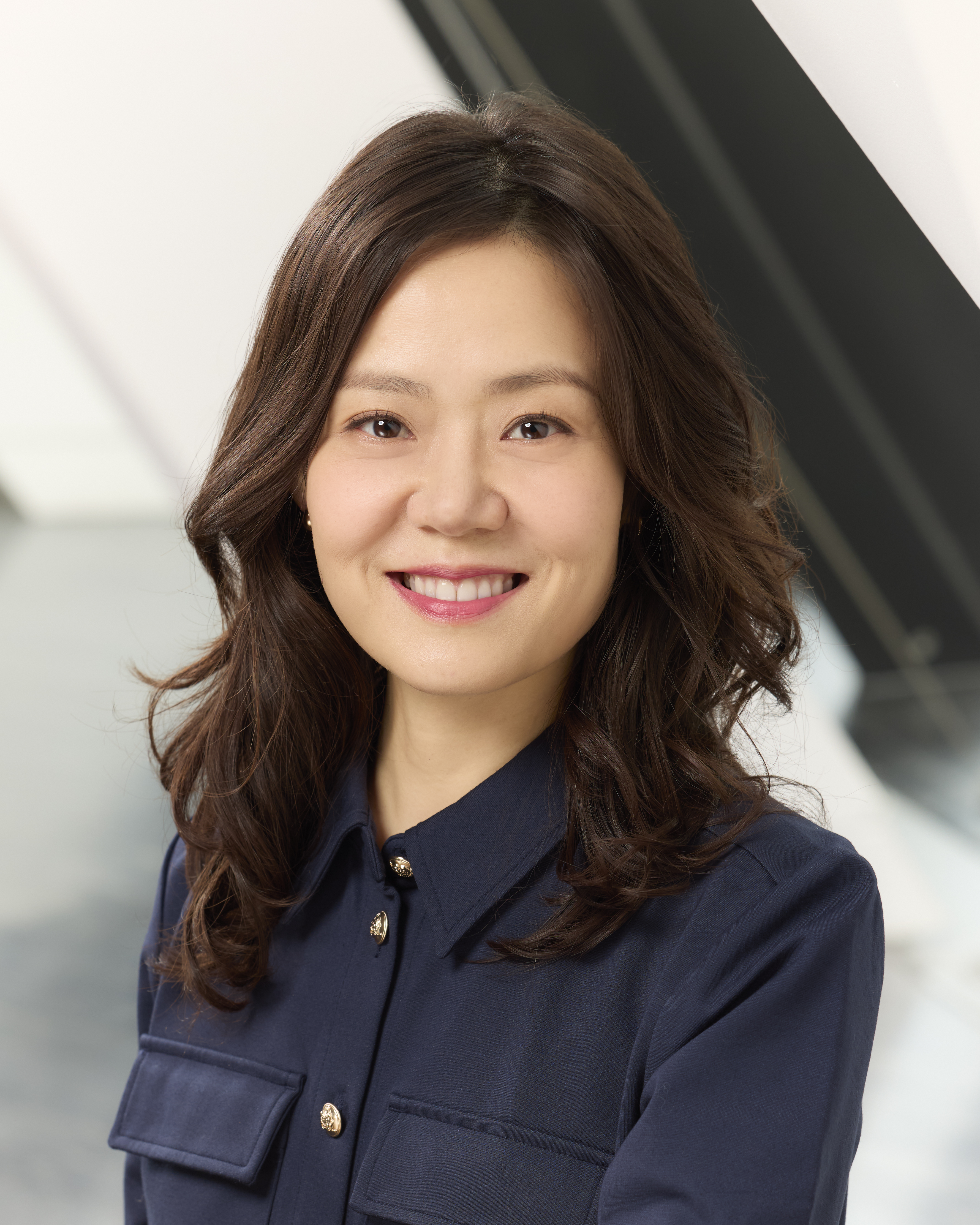 Portrait of a smiling woman with long wavy hair wearing a dark blue button-up shirt.