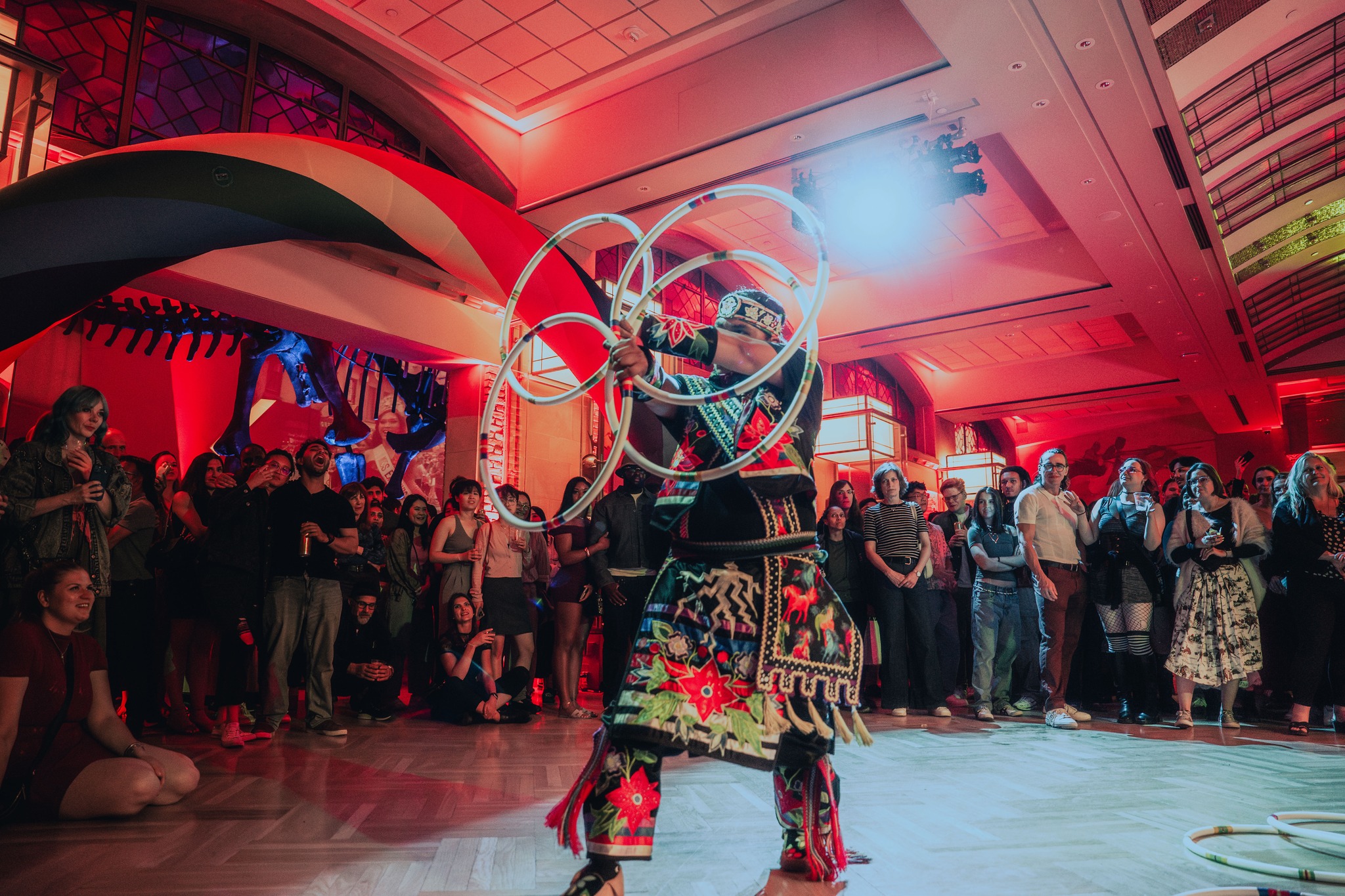 An Indigenous man in regailia dances with hoops in front of a crowd