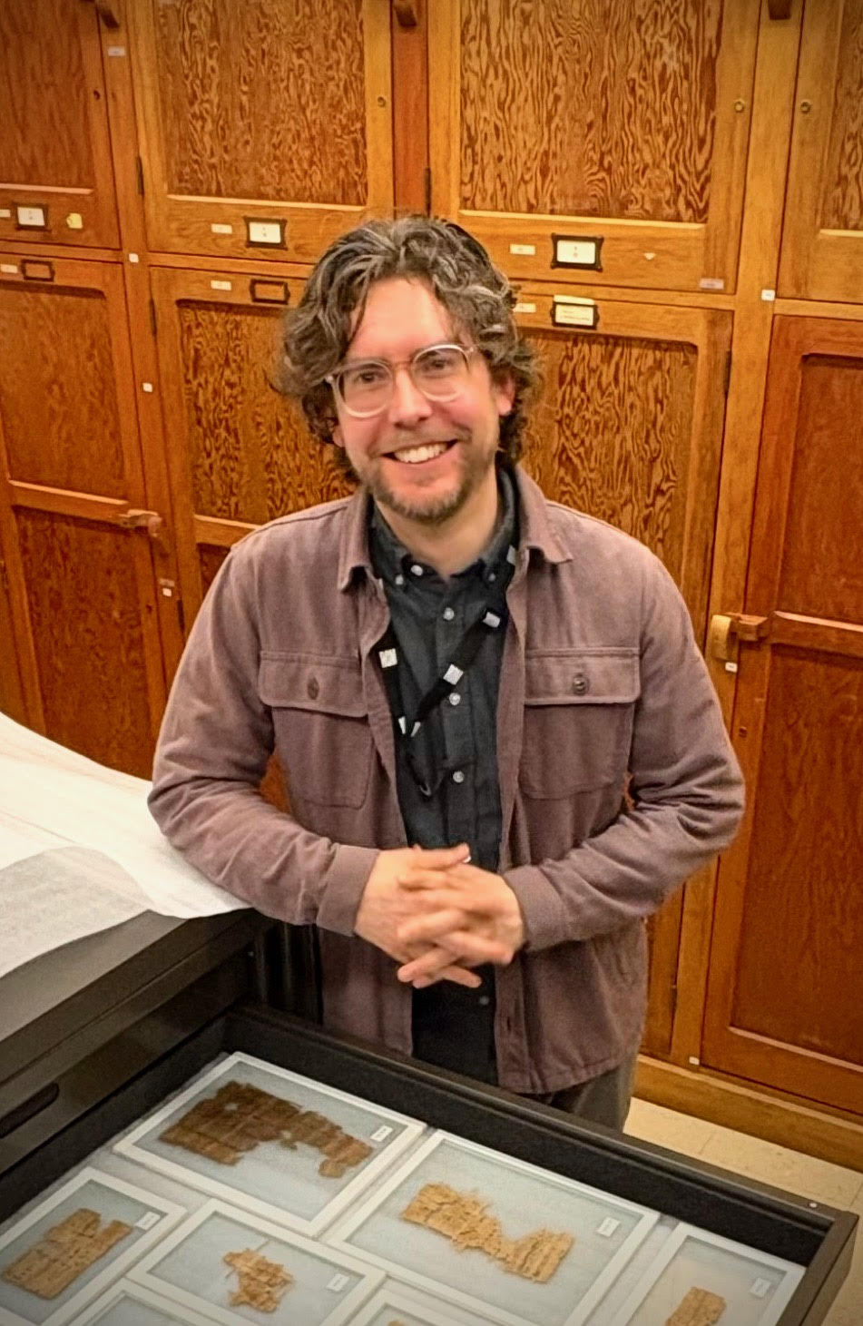 Dr. Gregory Fewster standing with clasped hands in front of museum drawers.