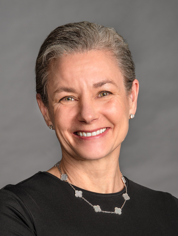 Portrait of a smiling woman with short gray hair wearing a black top and a necklace.