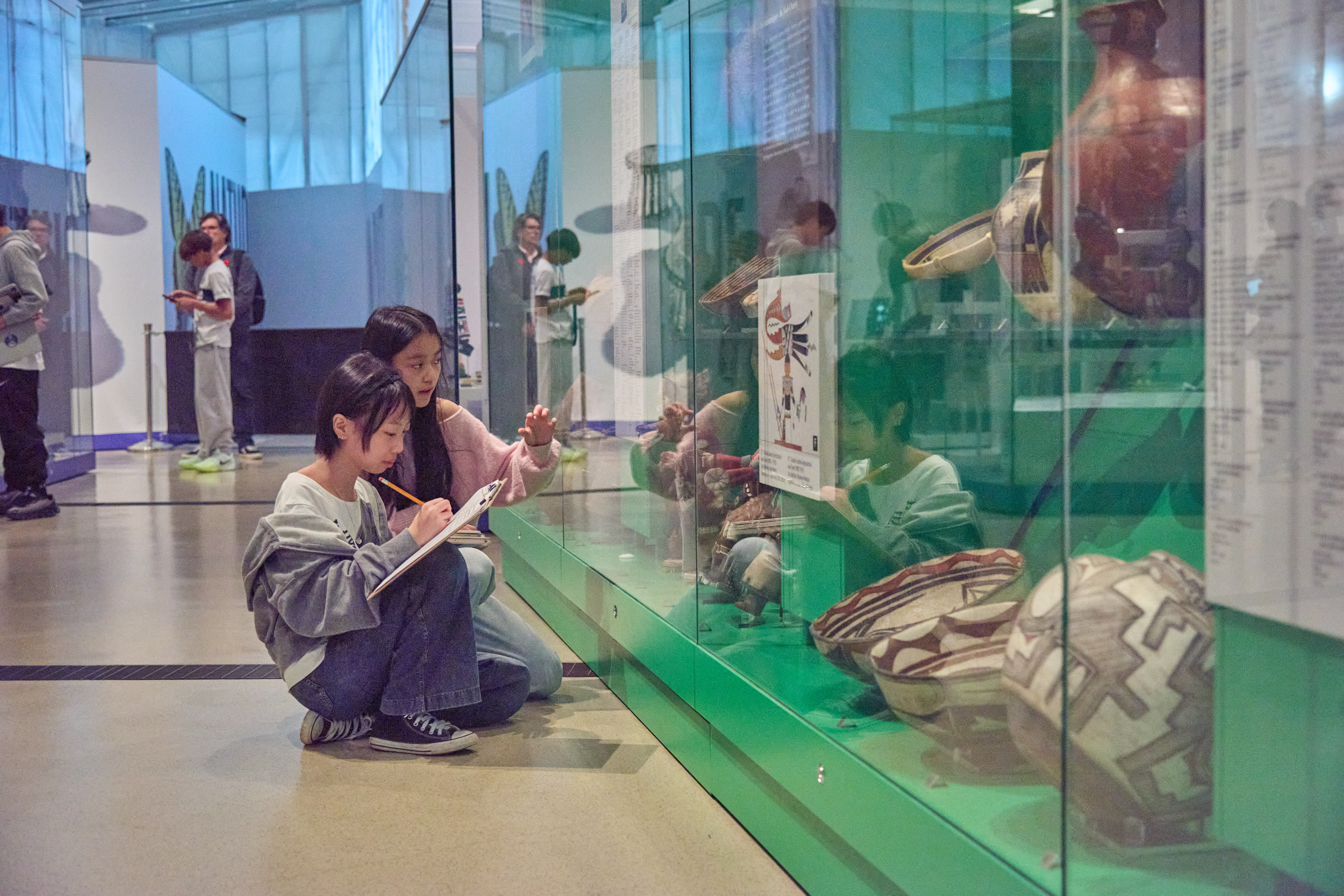 Students crouch in front of a museum case taking notes