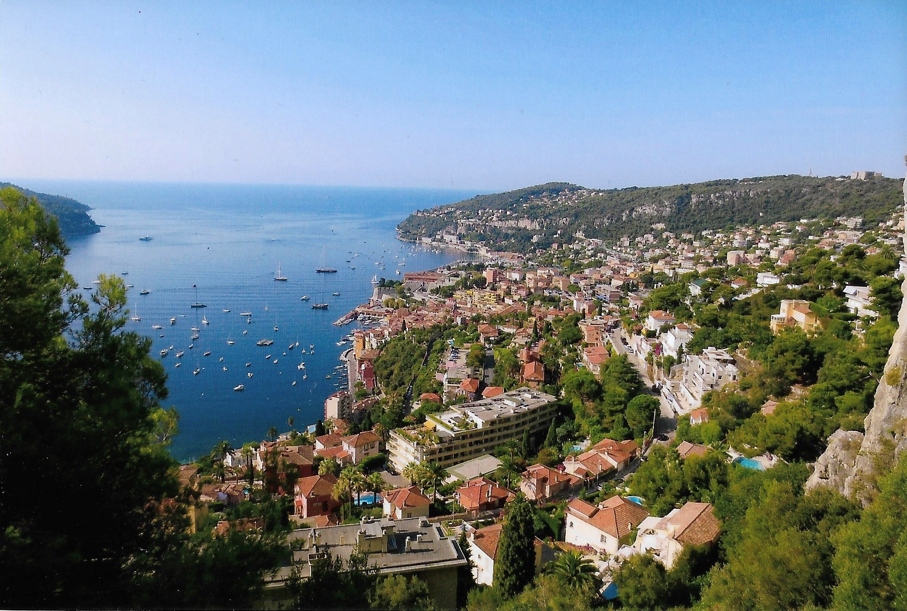 A picturesque coastal town with numerous buildings, and a beautiful, calm sea with several boats.