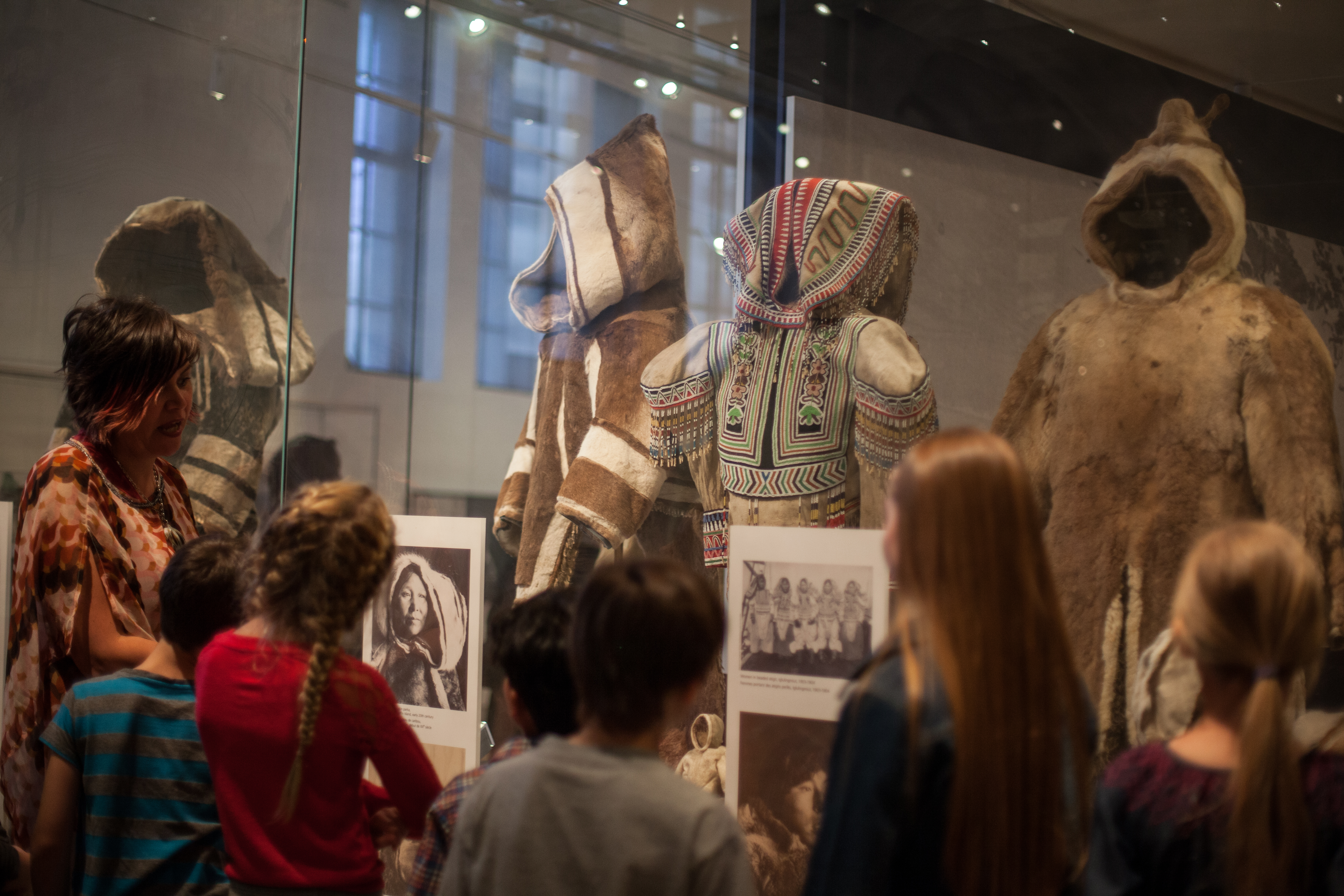 A teacher speaks to a group of students in front of a display case of sealskin parkas.
