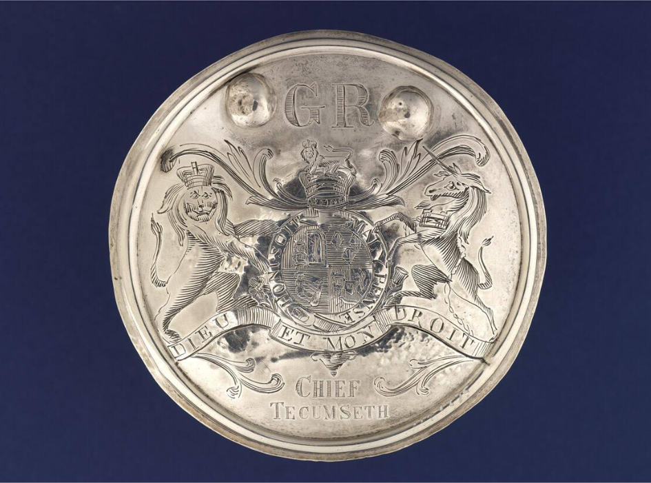 Round silver belt buckle with a coat of arms engraved in the centre, the letters G R at the top, and Chief Tecumseth at the bottom.