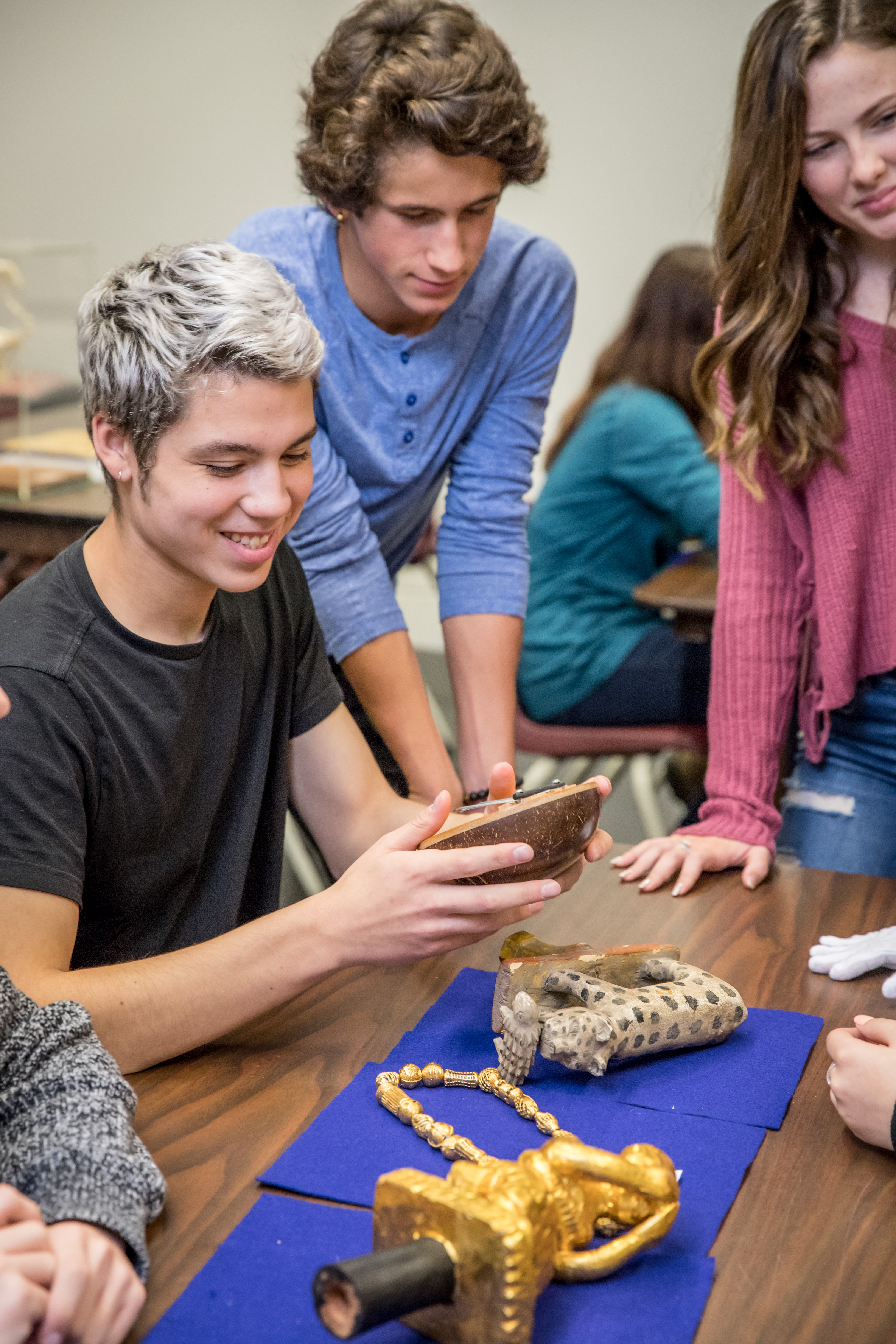 A smiling student examines an mbira (an African thumb piano), while two other students look on.