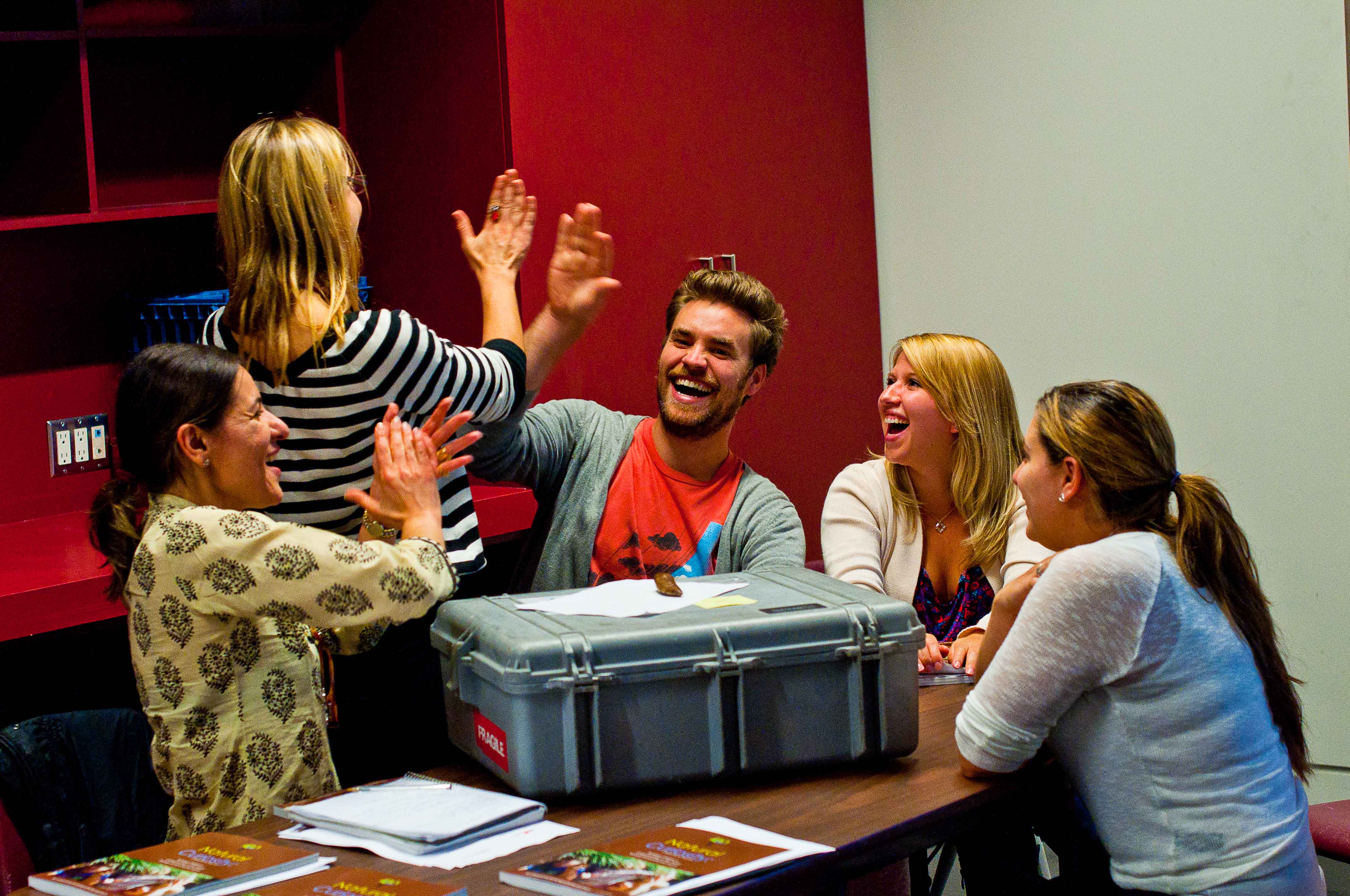 Teachers laugh and give each other high-fives around a table