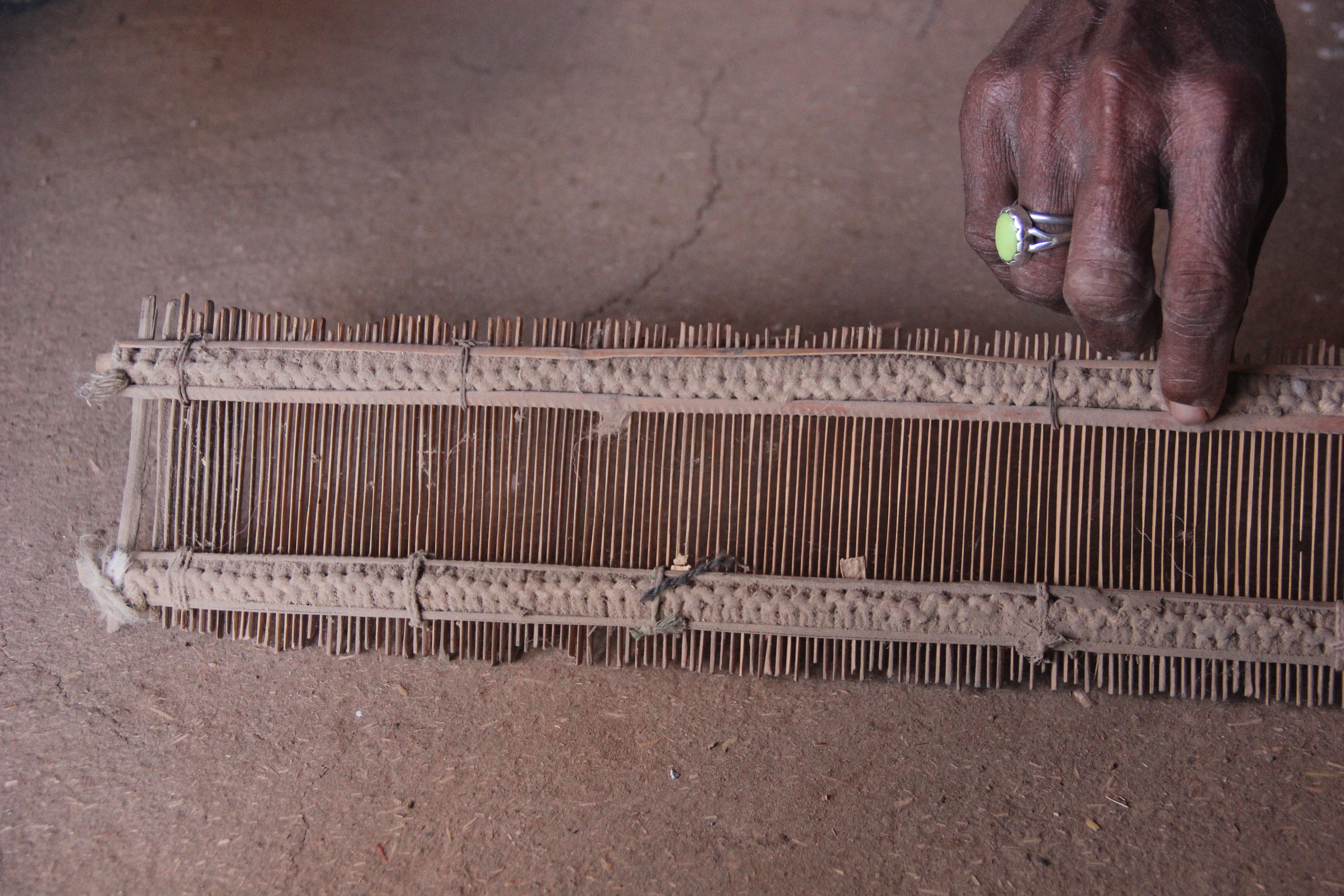 A hand with rings adjusting a rectangular frame of vertical wooden sticks.