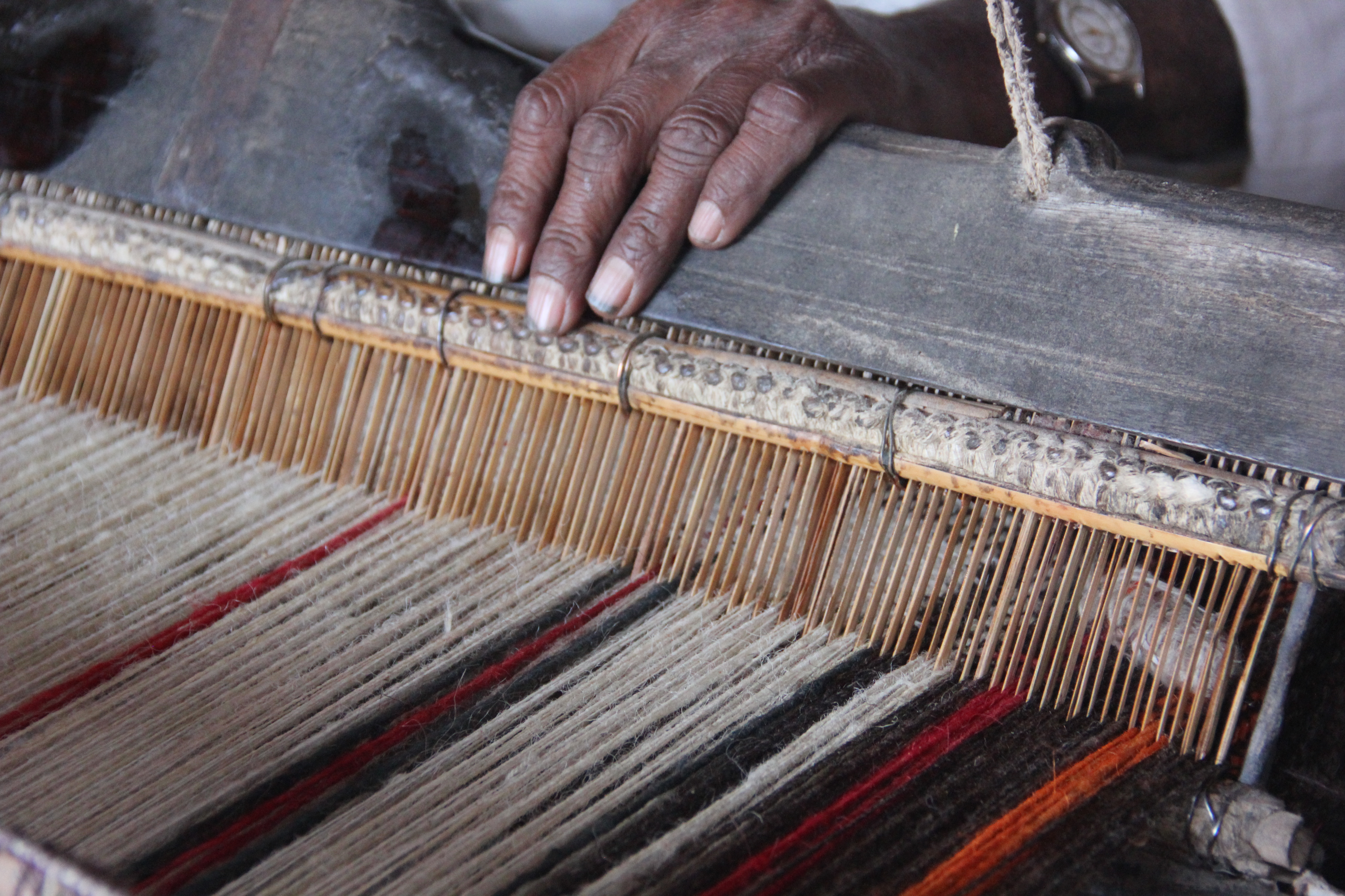 Close-up of hands weaving multicolored threads on a traditional loom.