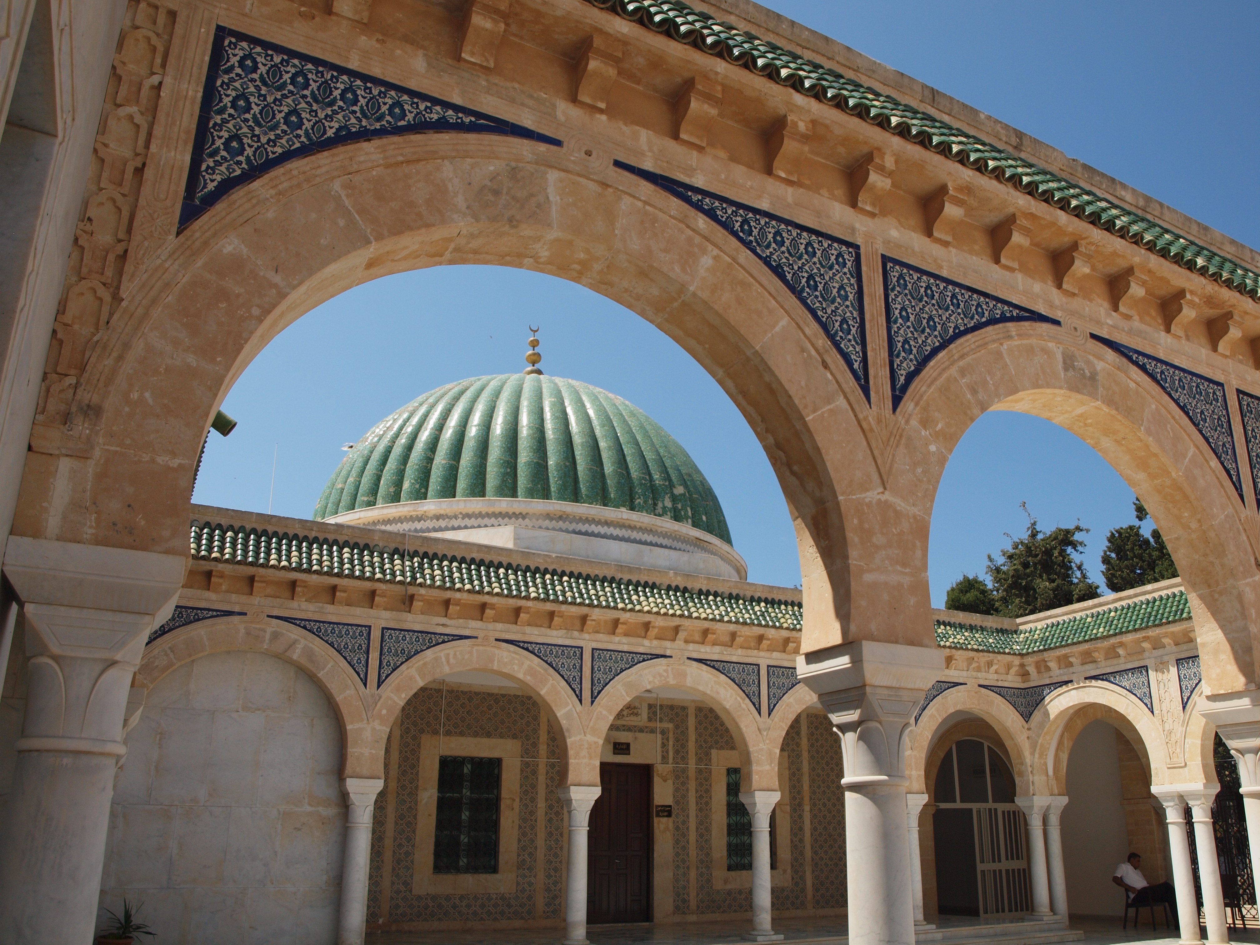 A beautiful, ornately decorated Islamic building with a domed roof and a blue tiled interior, under a clear blue sky.