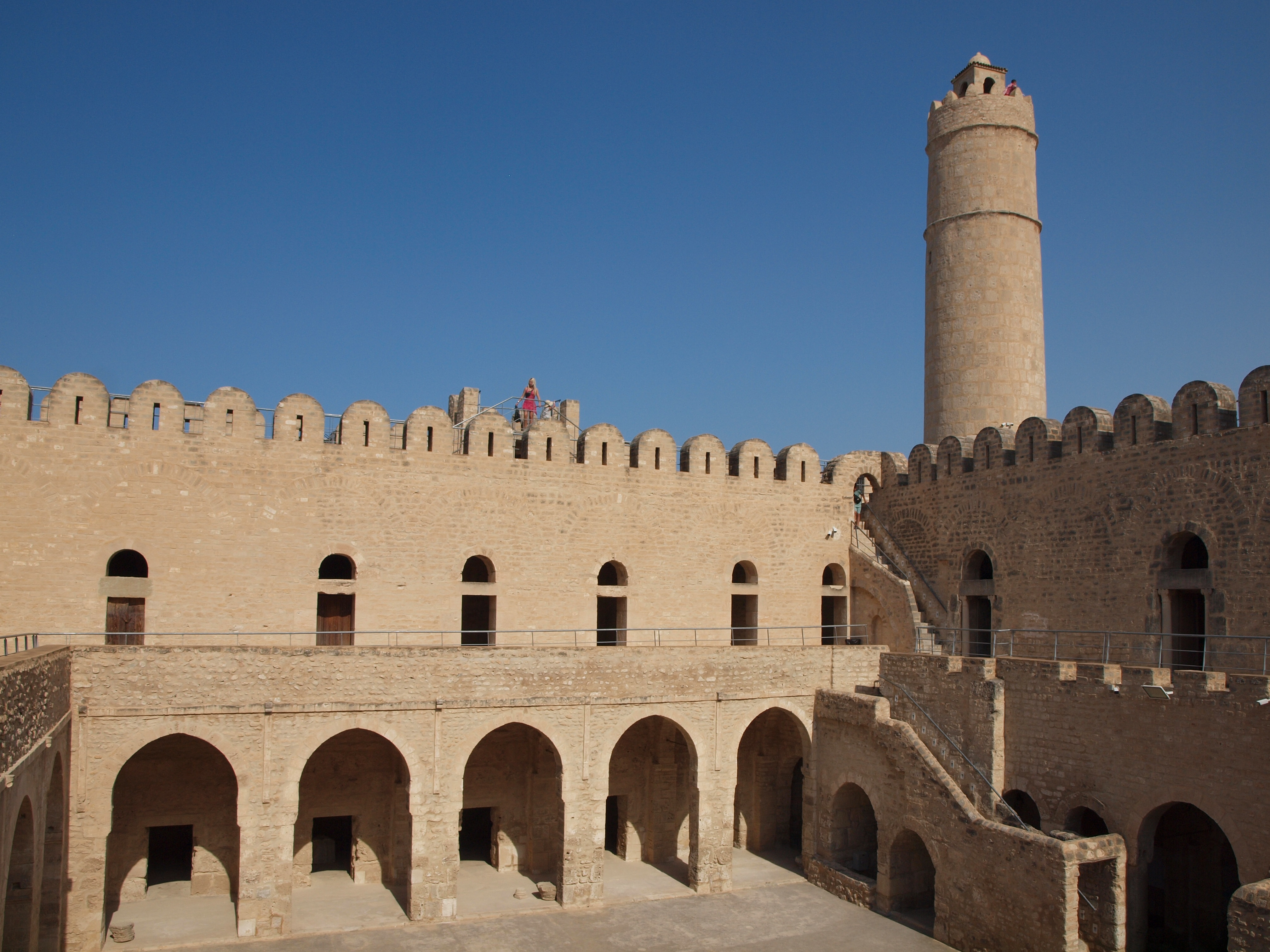 Alt text: An historic fortress with a tall, cylindrical tower under a clear blue sky.