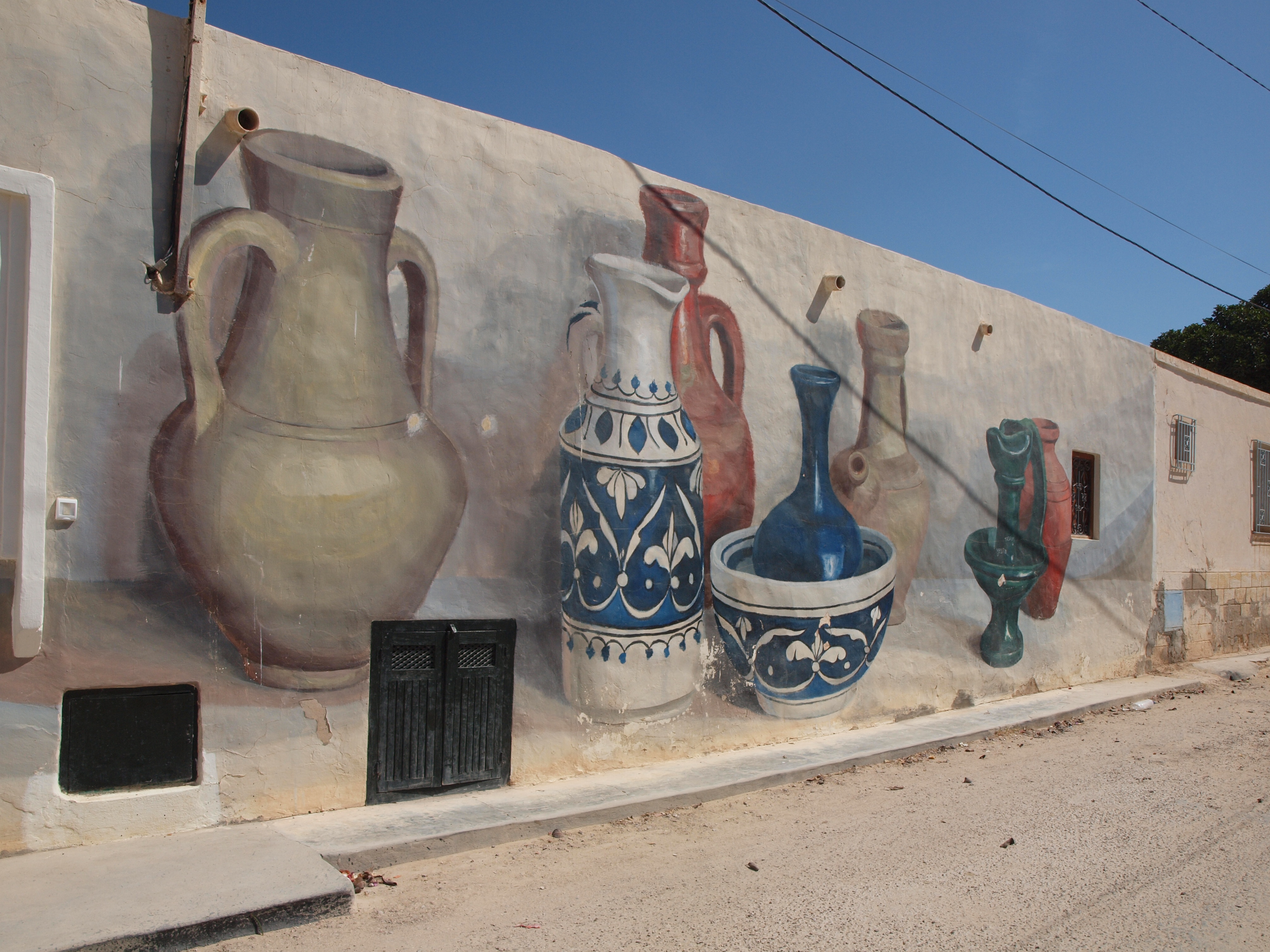 A wall mural featuring colourful, hand-painted ceramic jugs arranged in a symmetrical, abstract pattern against a clear blue sky.