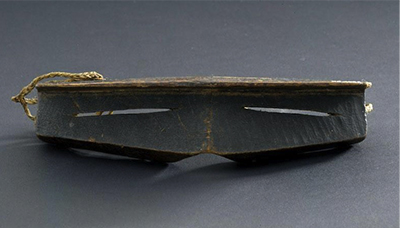 Iggaak (snow goggles) carved from wood with narrow horizontal slits for the eyes, and a string at the back.
