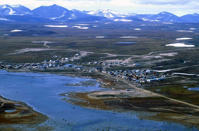 Historic coloured photograph of the landscape of the community of Clyde River, mountains, grass, small houses.