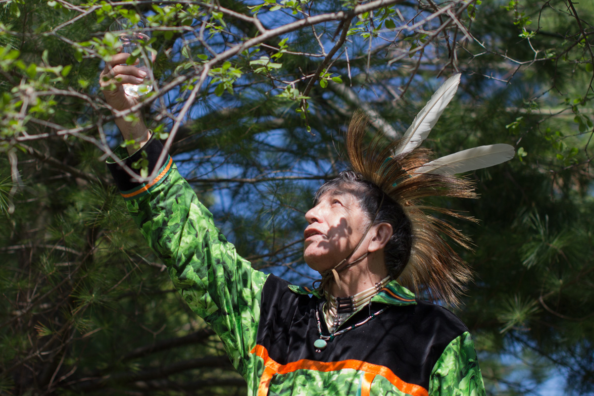 An indigenous man in traditional dress reaches upwards.