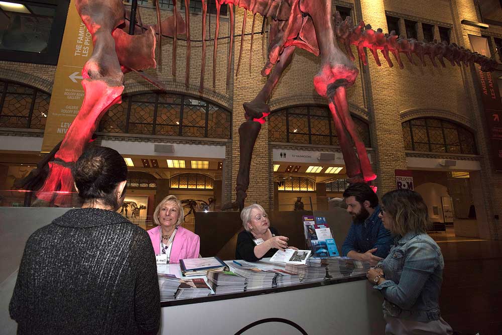 Visitors talking to DMV staff helpers at the information booth under Futolongkosaurus